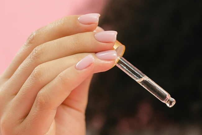 Frauenhand hält Pipette mit Vitamin D Tropfen